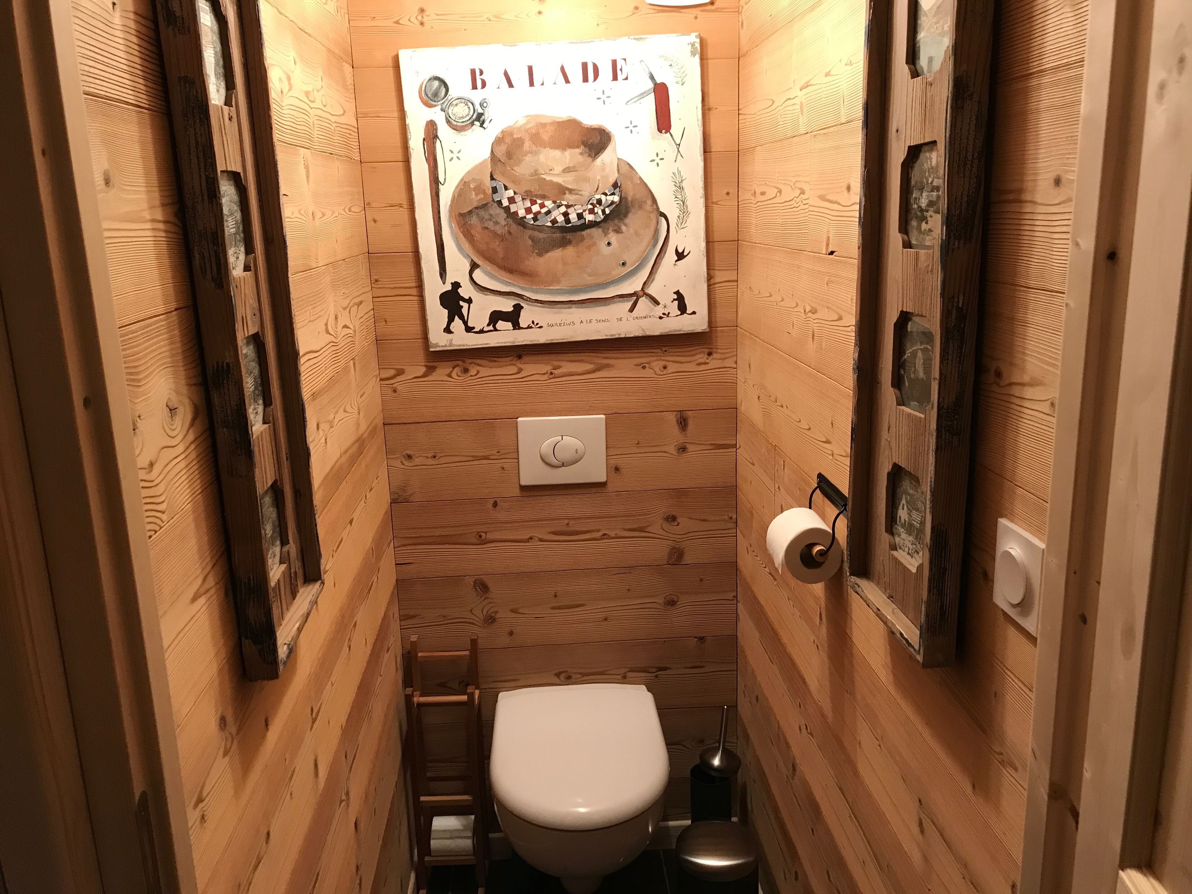 A small, wooden-paneled bathroom with a toilet, a ladder, and a poster on the wall.