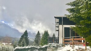 Un edificio moderno con balcón, rodeado de árboles cubiertos de nieve y un cielo despejado.