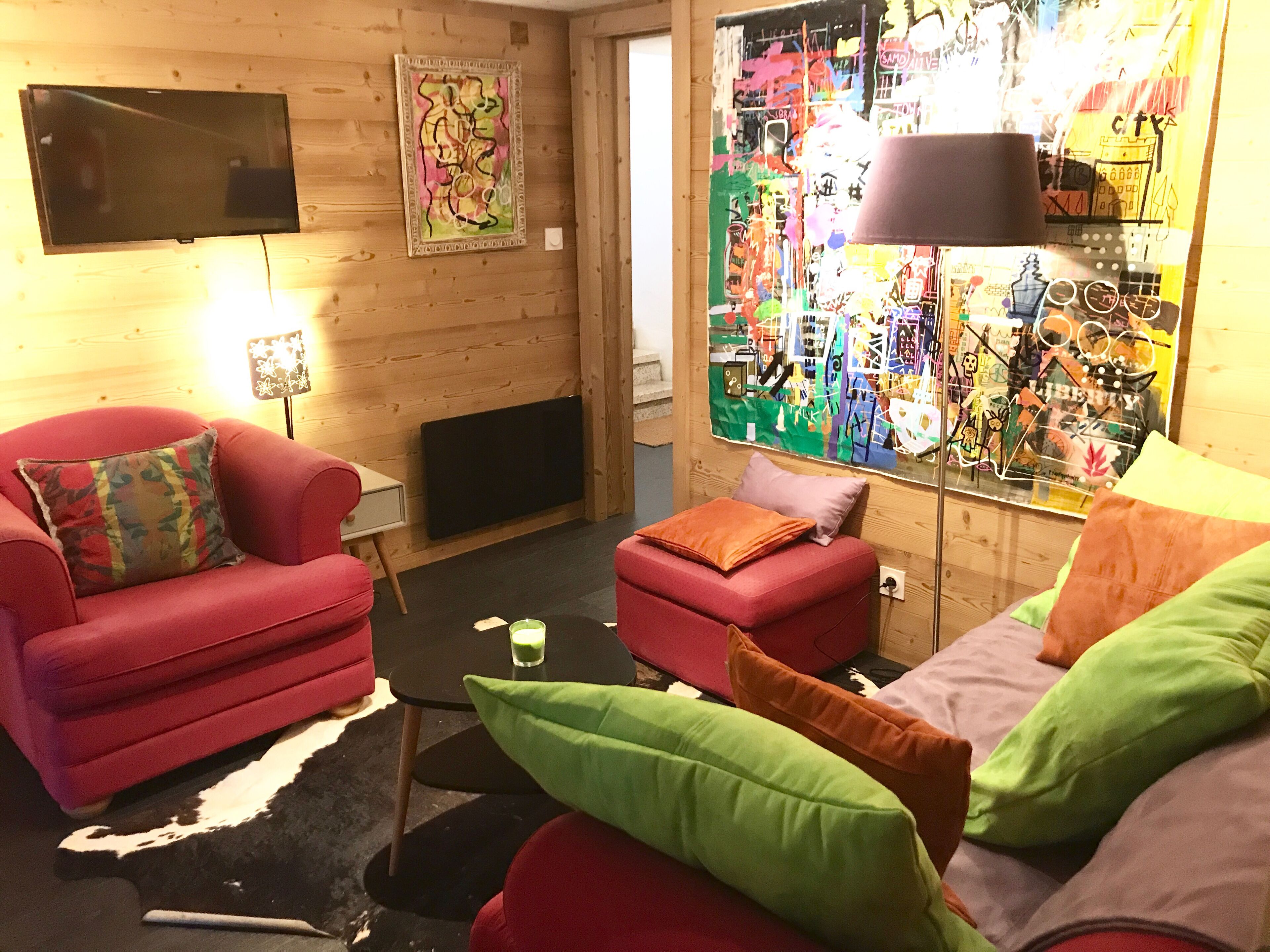 En hyggelig stue med en rød sofa, en lille skammel og et fjernsyn på væggen.