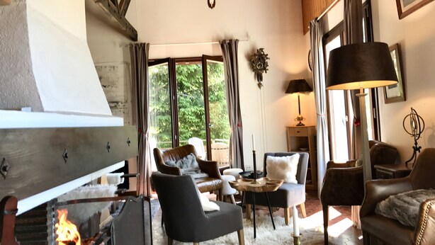 Una sala de estar acogedora con chimenea, asientos cómodos y ventanas amplias con vistas al verdor.