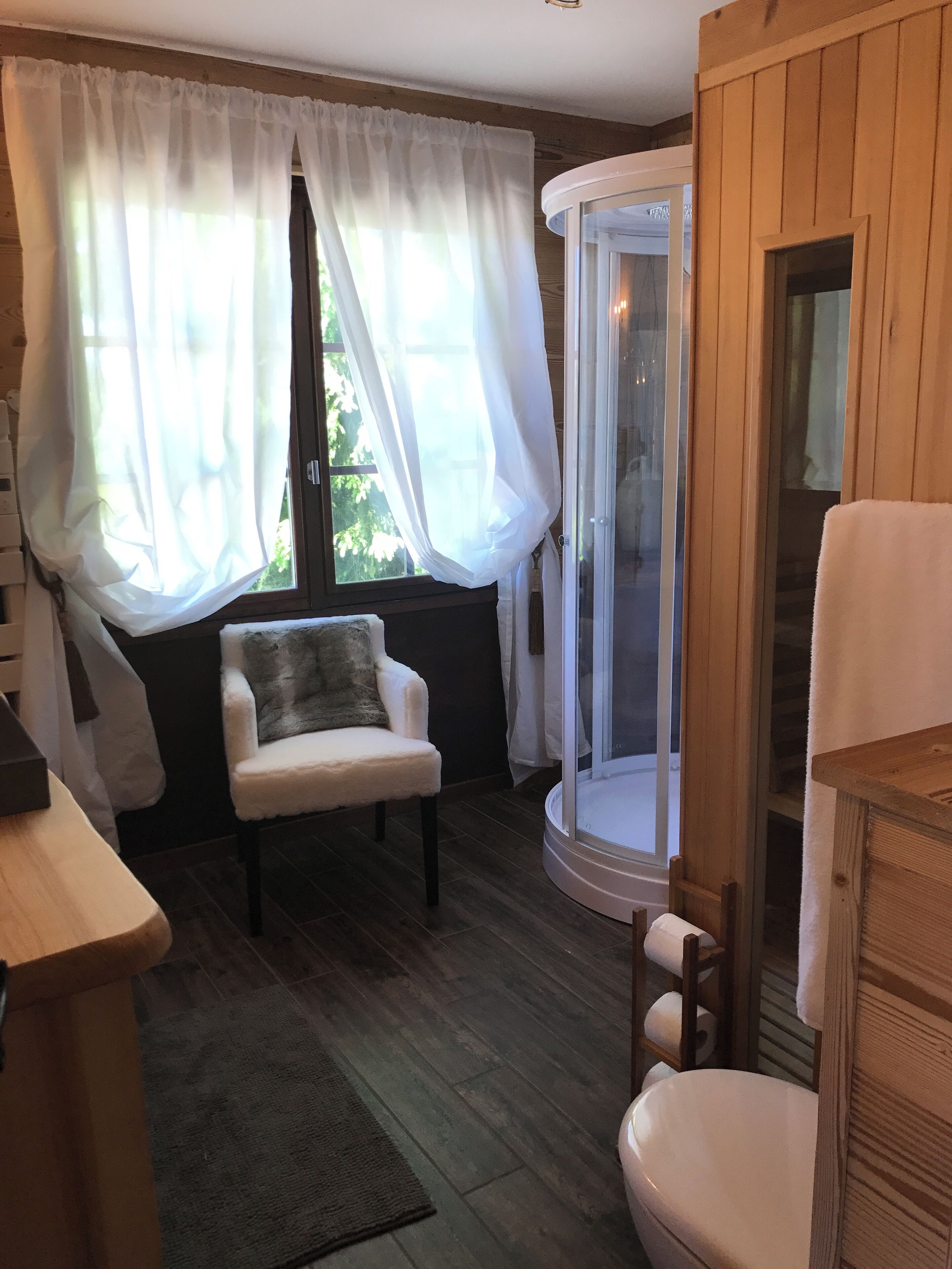 A cozy room with a wooden floor, a white chair, a small table, and a glass shower enclosure.