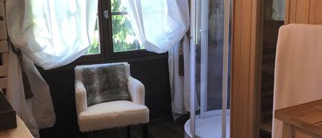 A cozy room with a wooden floor, a white chair, a small table, and a glass shower enclosure.