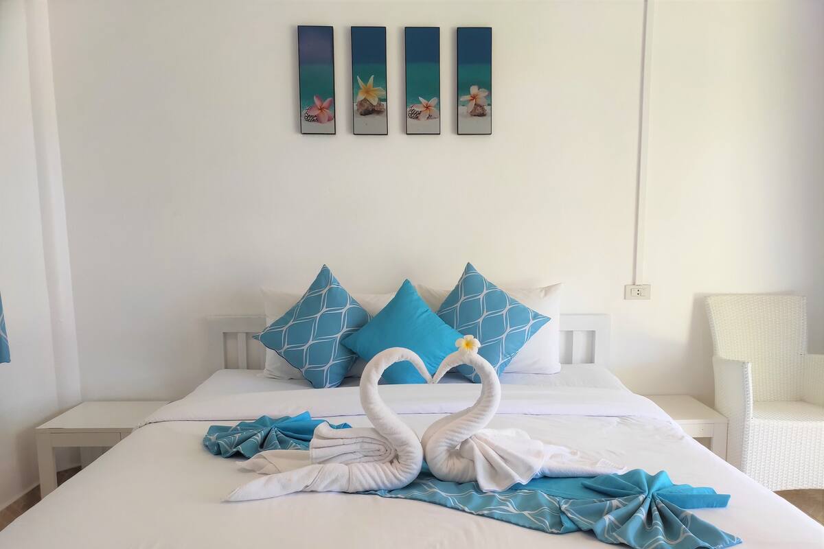 A neatly made bed with blue and white pillows, a white headboard, and a wall with four framed pictures.
