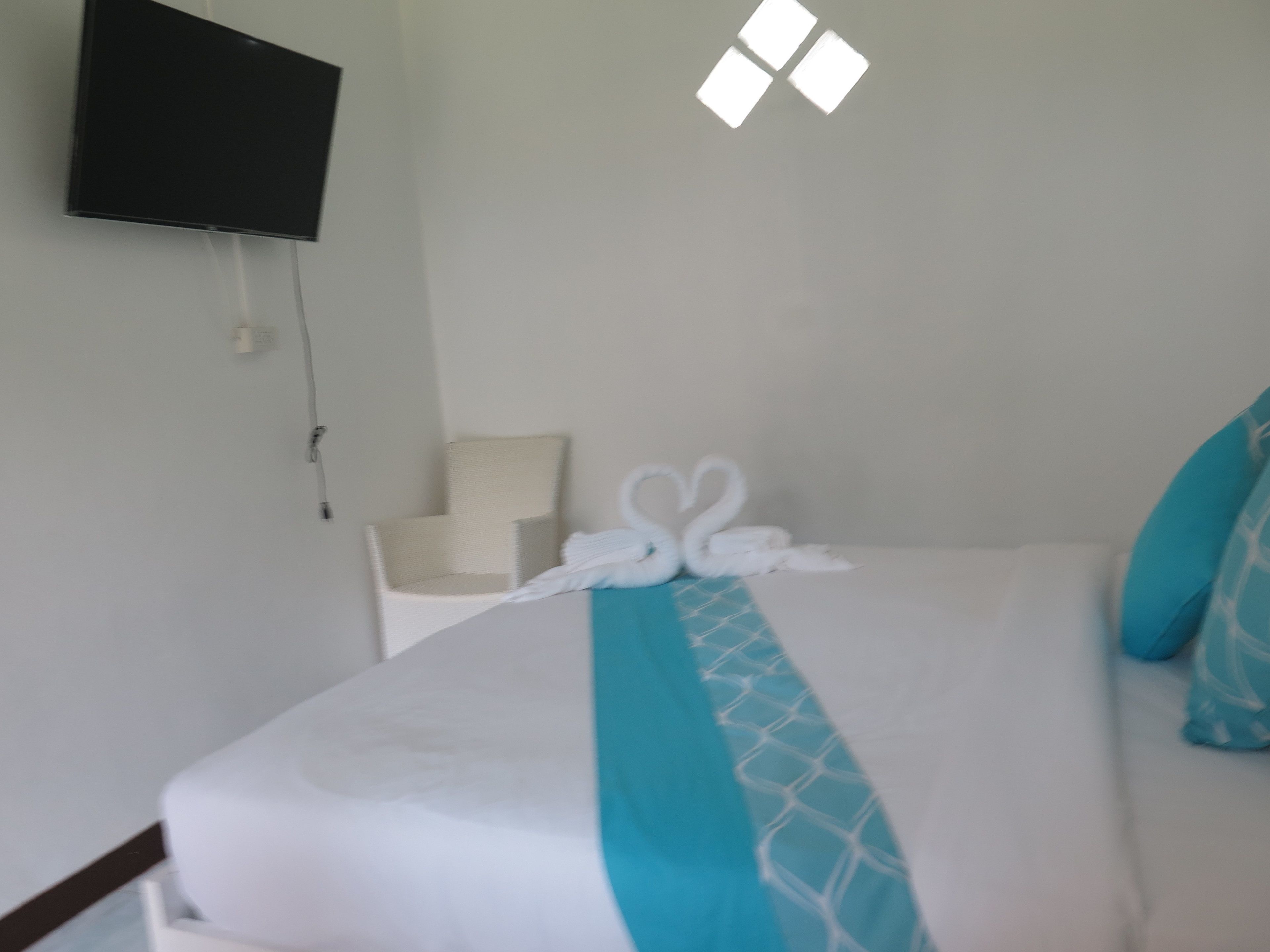 A hotel room with a bed, a chair, a TV mounted on the wall, and a window with blinds.