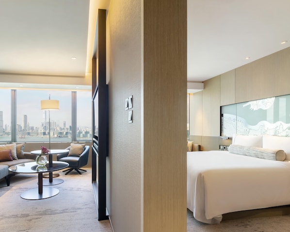 Una habitación de hotel moderna con una cama grande, vistas a la ciudad, una mesa de centro redonda y un sofá.
