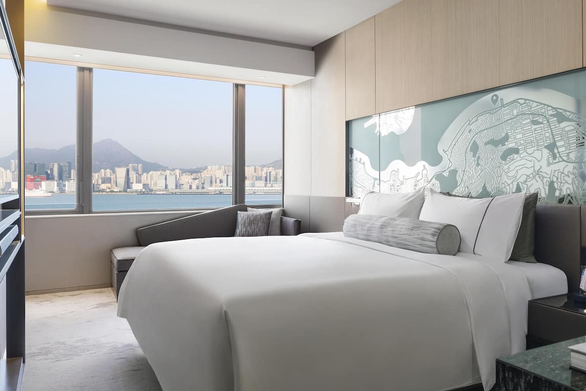 Habitació d'hotel moderna amb un llit gran, zona de seients i vista a la ciutat a través de grans finestres.