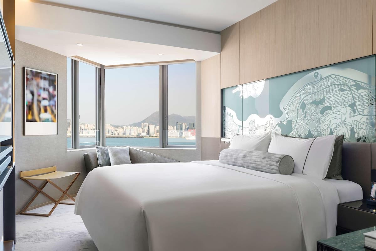 Una habitació d'hotel moderna amb un llit gran, un escriptori i vista a un paisatge urbà a través de grans finestres.