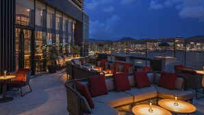 An outdoor seating area with wicker furniture and red cushions, overlooking a cityscape at dusk. - Hyatt Centric Victoria Harbour Hong Kong (Hong Kong)