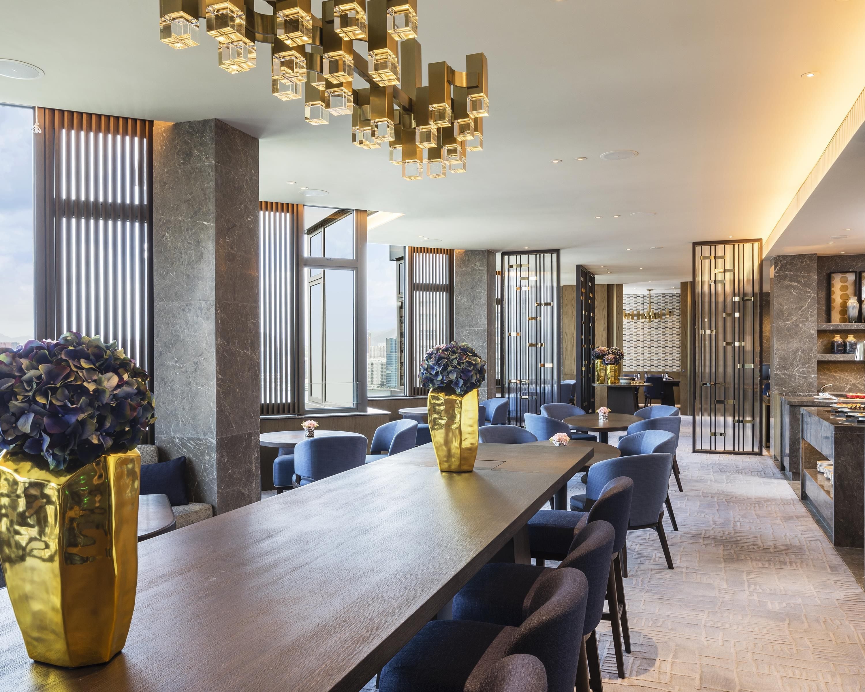 A modern hotel lobby with a long wooden reception desk, seating area, and a decorative ceiling light fixture.