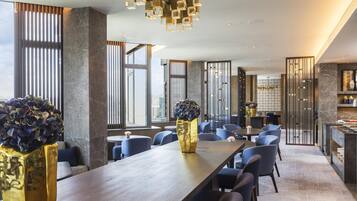 Een moderne hotellobby met een lange houten receptiebalie, een zithoek en een decoratieve plafondlamp.