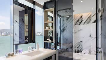 A modern bathroom with a large mirror, two sinks, a shower, and a view of the city.