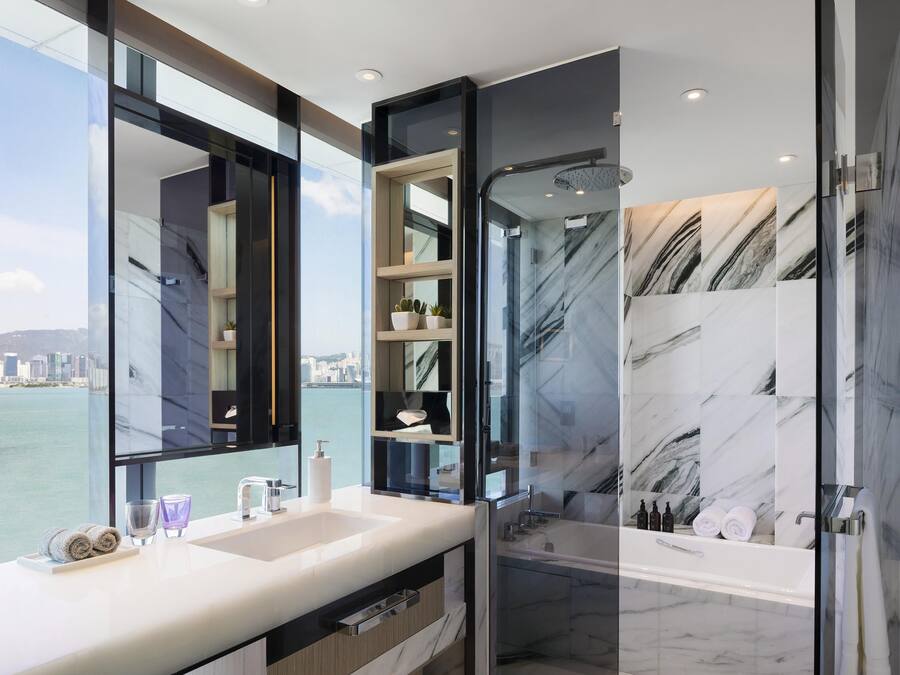 A modern bathroom with a large mirror, two sinks, a shower, and a view of the city.
