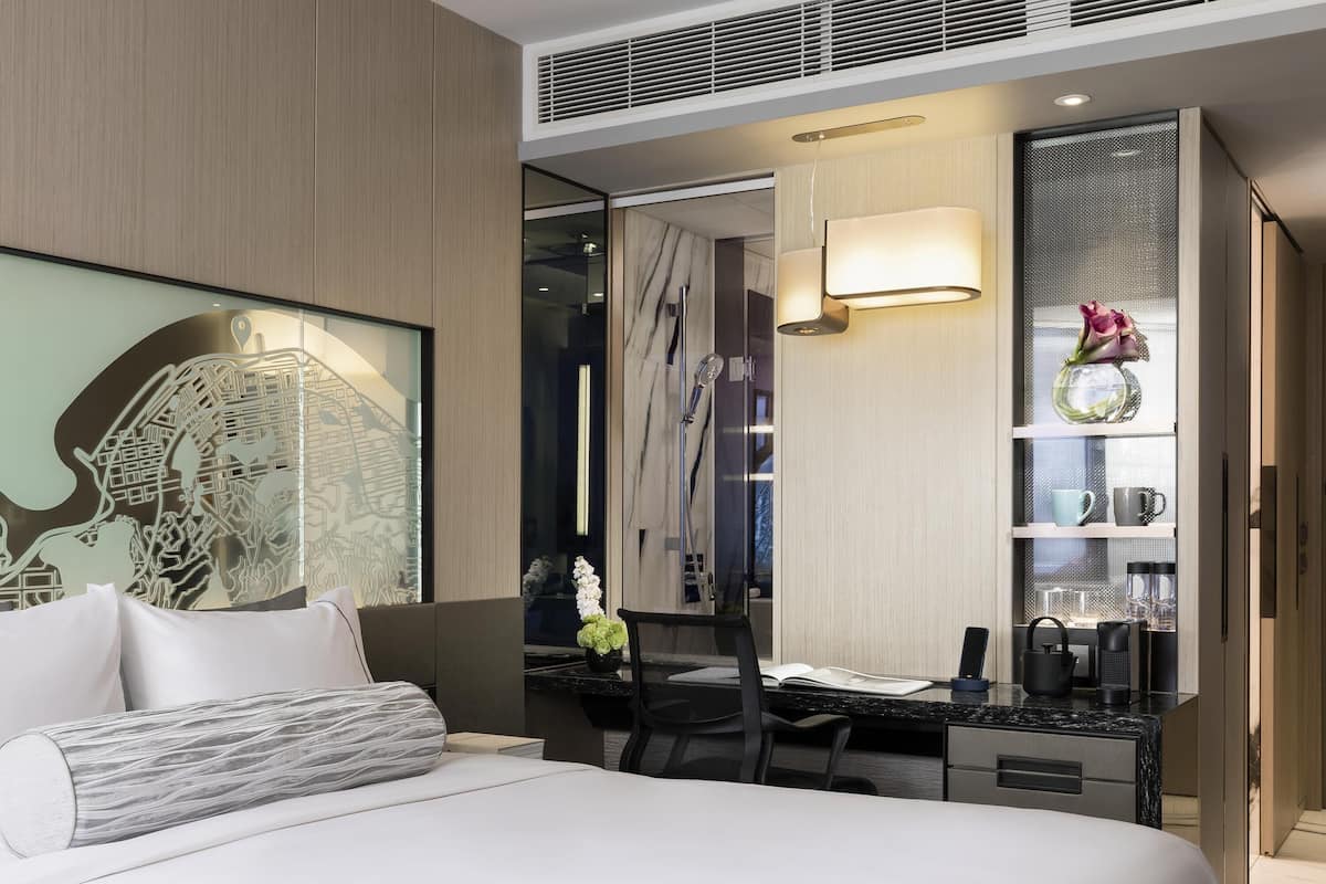 Habitació d'hotel moderna amb un llit gran, una taula de treball, una cadira, un mirall i una obra decorativa a la paret.