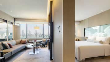 Una habitación de hotel moderna con una cama grande, un sofá, una mesita de centro y vistas a la ciudad a través de amplios ventanales.
