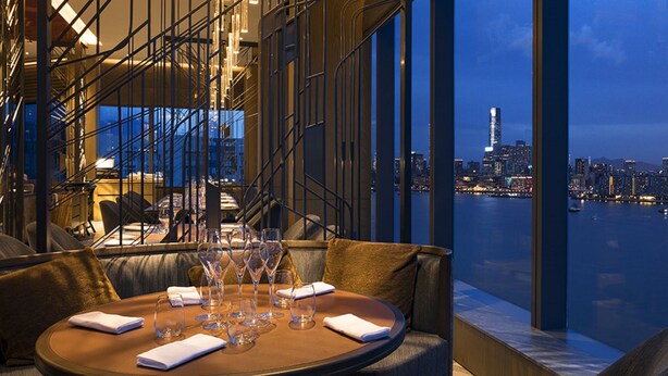 A dining area with a table set for four, overlooking a cityscape and a body of water at dusk. - Hyatt Centric Victoria Harbour Hong Kong (Hong Kong)