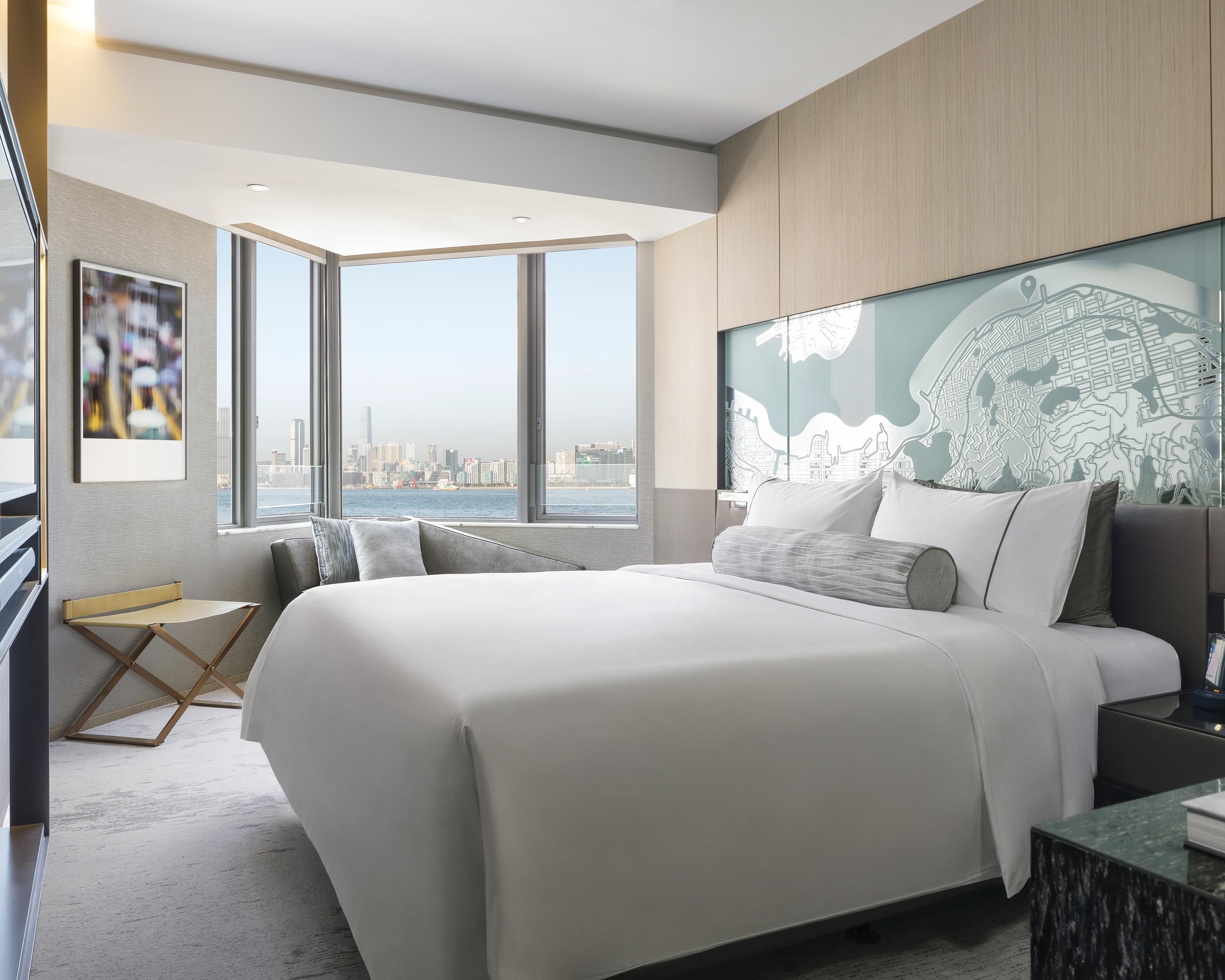A modern hotel room with a large bed, a desk, and a view of the city skyline.