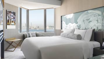 A modern hotel room with a large bed, a desk, and a view of the city skyline.