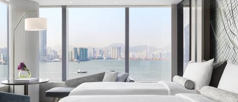 A modern hotel room with a large window, a bed, a sofa, and a desk with a lamp.