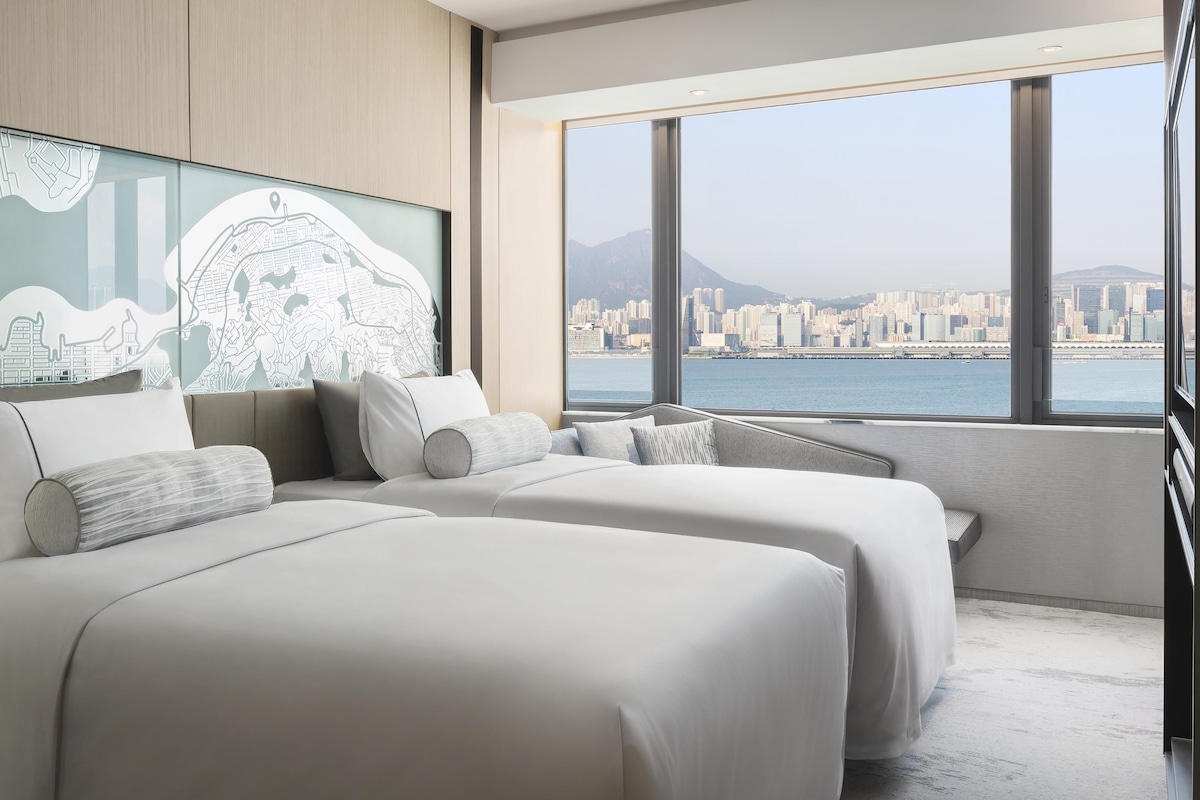 Una habitación de hotel moderna con un ventanal que ofrece vistas a la ciudad, una cama con ropa de cama blanca y un mapa colgado en la pared.