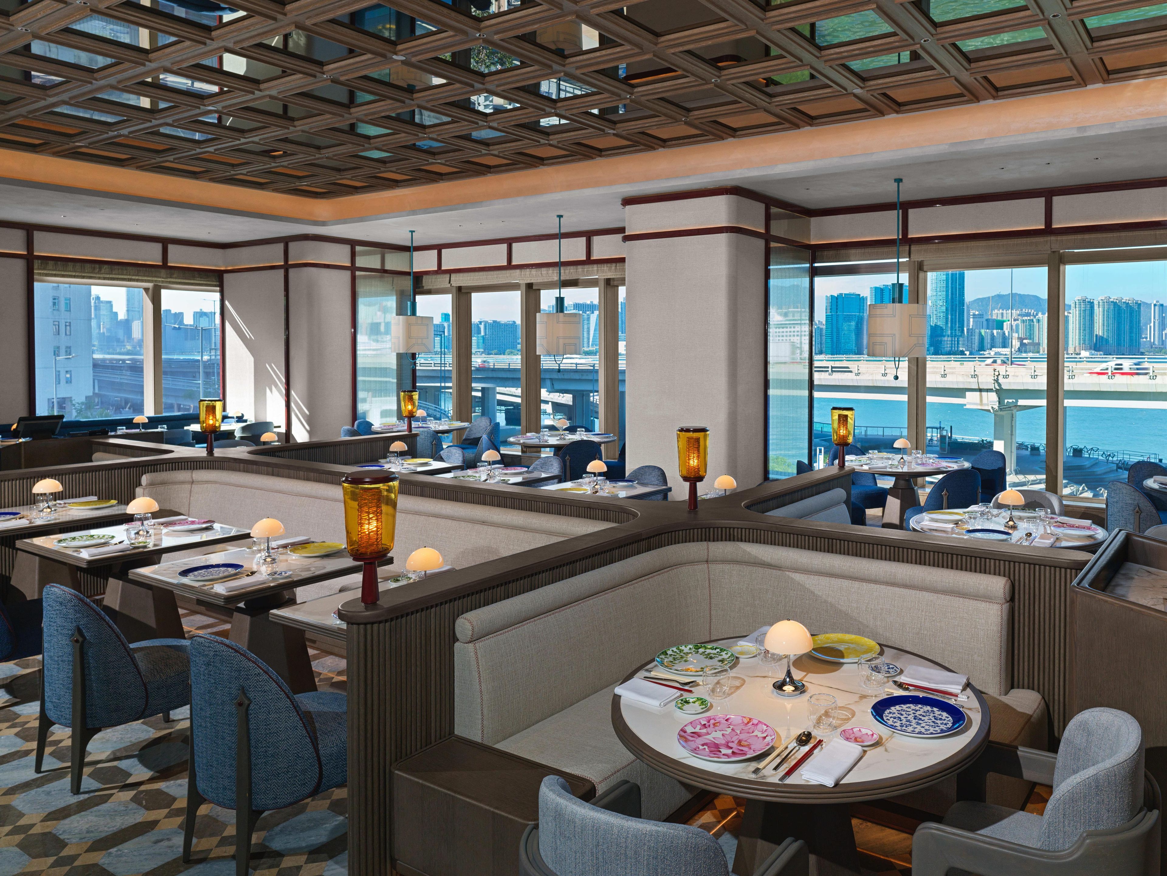 A modern restaurant with high-rise city views, partitioned seating, and ambient lighting.