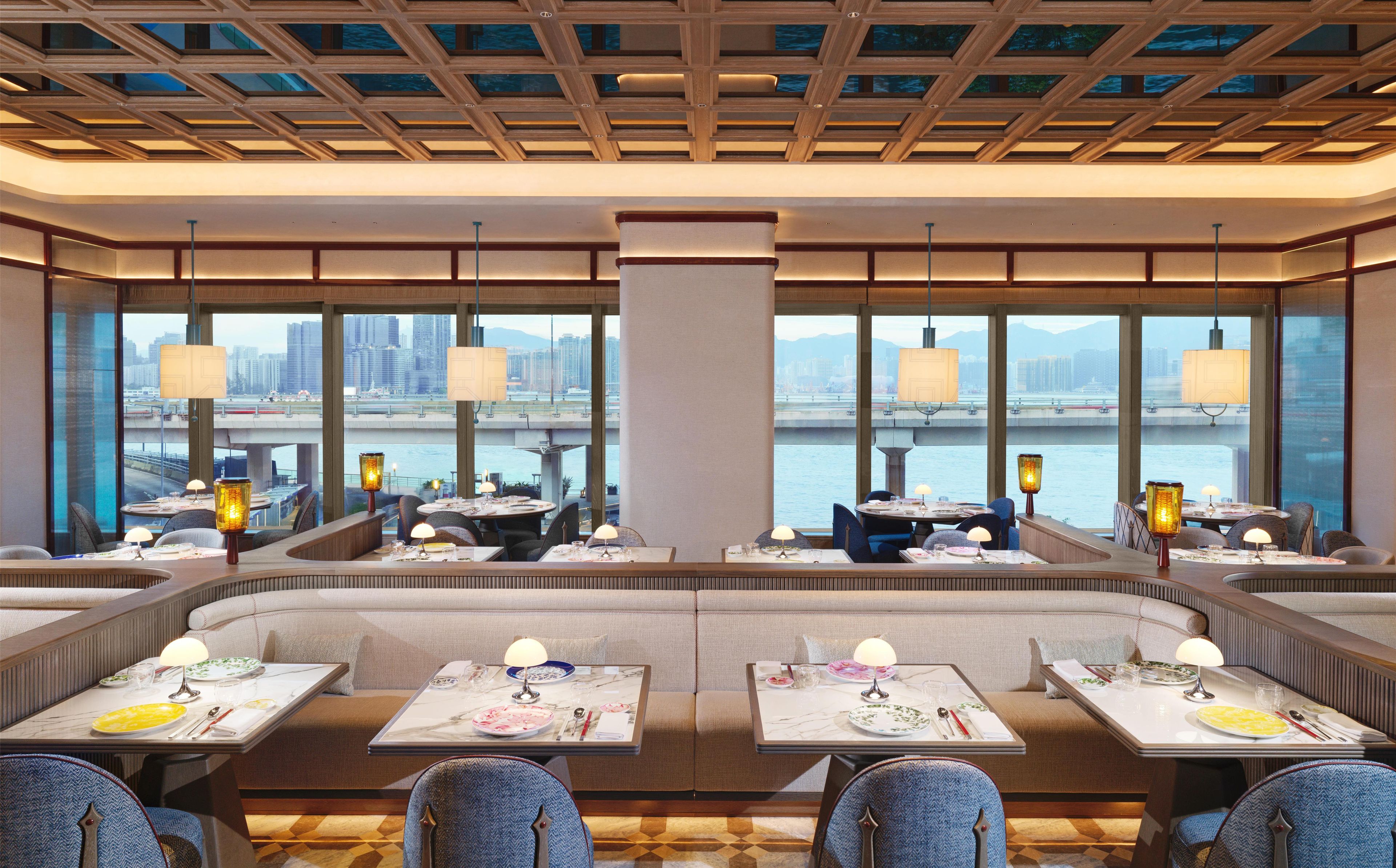 A restaurant with multiple tables and booths, large windows with a city view, and hanging lamps.