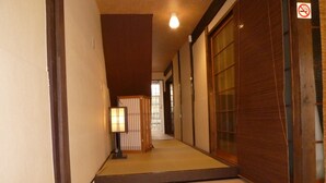 Un intérieur japonais traditionnel avec un sol recouvert de tatamis, un banc en bois et un meuble à chaussures contenant différents types de chaussures.