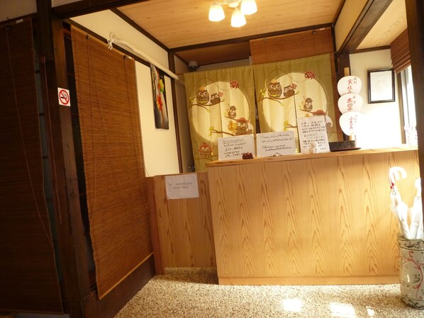 A hotel reception area with a wooden counter, a 'No Admittance Staff Only' sign, and a 'Hotel Reception' sign with contact numbers.