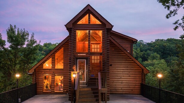 A log cabin with a welcoming entrance, a staircase leading to the main floor, and a view of the surrounding forest.