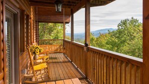 A wooden deck with a wooden bench and a vase of sunflowers, overlooking a mountainous landscape.