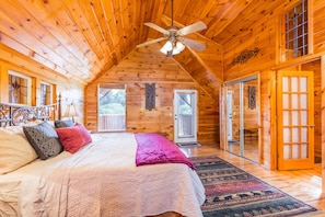 A cozy wooden cabin bedroom with a bed, a ceiling fan, and a view of the outdoors through a door.