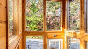 A wooden cabin with large windows, a staircase, and a view of trees.