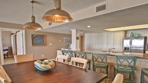A spacious dining area with a wooden table and chairs, a bowl of decorative items, and pendant lighting. - Beach More, Worry Less: 10% Off on 7+ Night Stays! (South Padre Island)