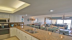 A modern kitchen with granite countertops, stainless steel appliances, and a dining area with a view. - Beach More, Worry Less: 10% Off on 7+ Night Stays! (South Padre Island)