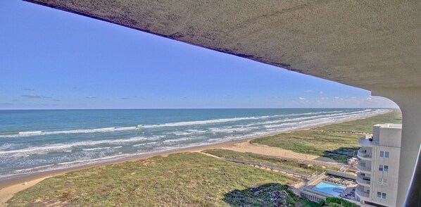 Blick vom Balkon auf den Strand und das Meer, mit Blick auf ein Hotelgebäude.