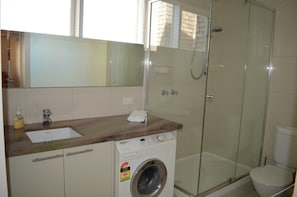 A bathroom with a washing machine, a sink, and a glass-enclosed shower. - Twin Towers 504B (Mount Buller)