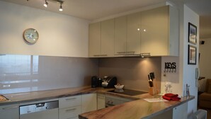 A modern kitchen with a built-in dishwasher, a coffee machine, and a toaster. There is a clock on the wall and a set of knives on the counter. - Twin Towers 504B (Mount Buller)