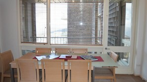 A dining area with a table and chairs, large windows with blinds, and a view of a building outside. - Twin Towers 504B (Mount Buller)