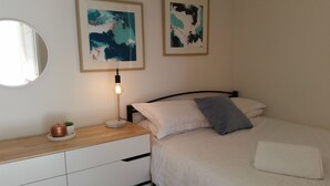 A bedroom with a bed, a bedside table with a lamp, a mirror, and two abstract paintings on the wall. - Twin Towers 504B (Mount Buller)