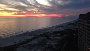 Une vue sur la côte, avec une jetée qui s’avance dans la mer, un bâtiment situé à côté de la plage et un coucher de soleil en arrière-plan.