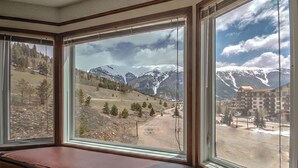Une pièce dotée d’une grande fenêtre donnant sur un paysage montagneux et un bâtiment.