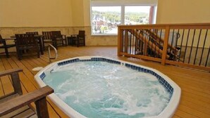 Un bain à remous dans une pièce au plancher en bois, avec une vue dégagée grâce à de grandes fenêtres et une balustrade en bois.