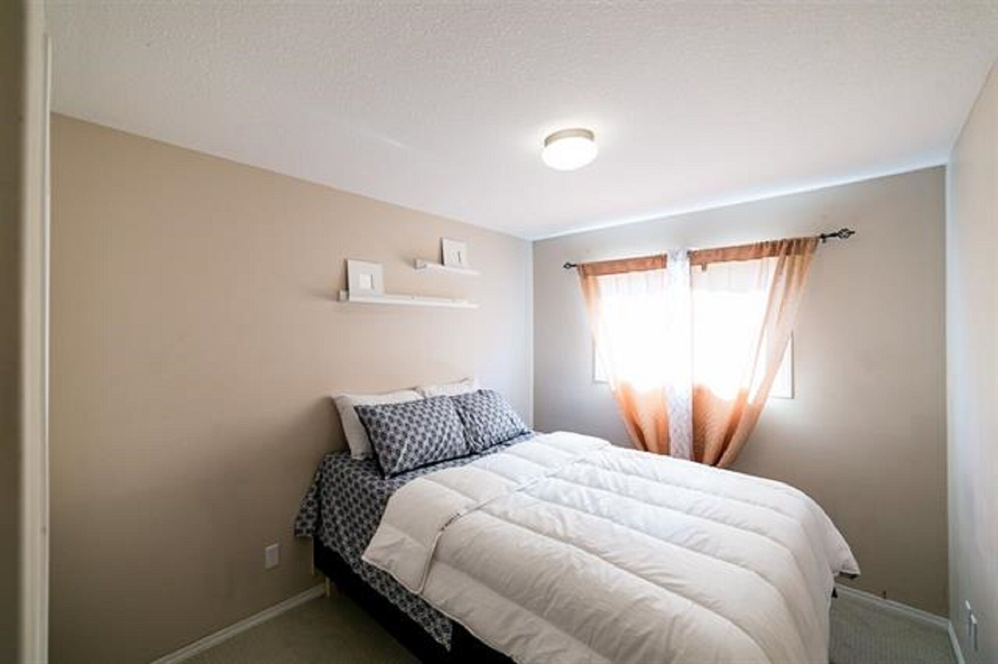 A bedroom with a bed, a window with curtains, and a ceiling light.