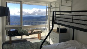 A bedroom with a bunk bed, a desk, a chair, and a large window offering a mountain view. - Twin Towers 701A (Mount Buller)