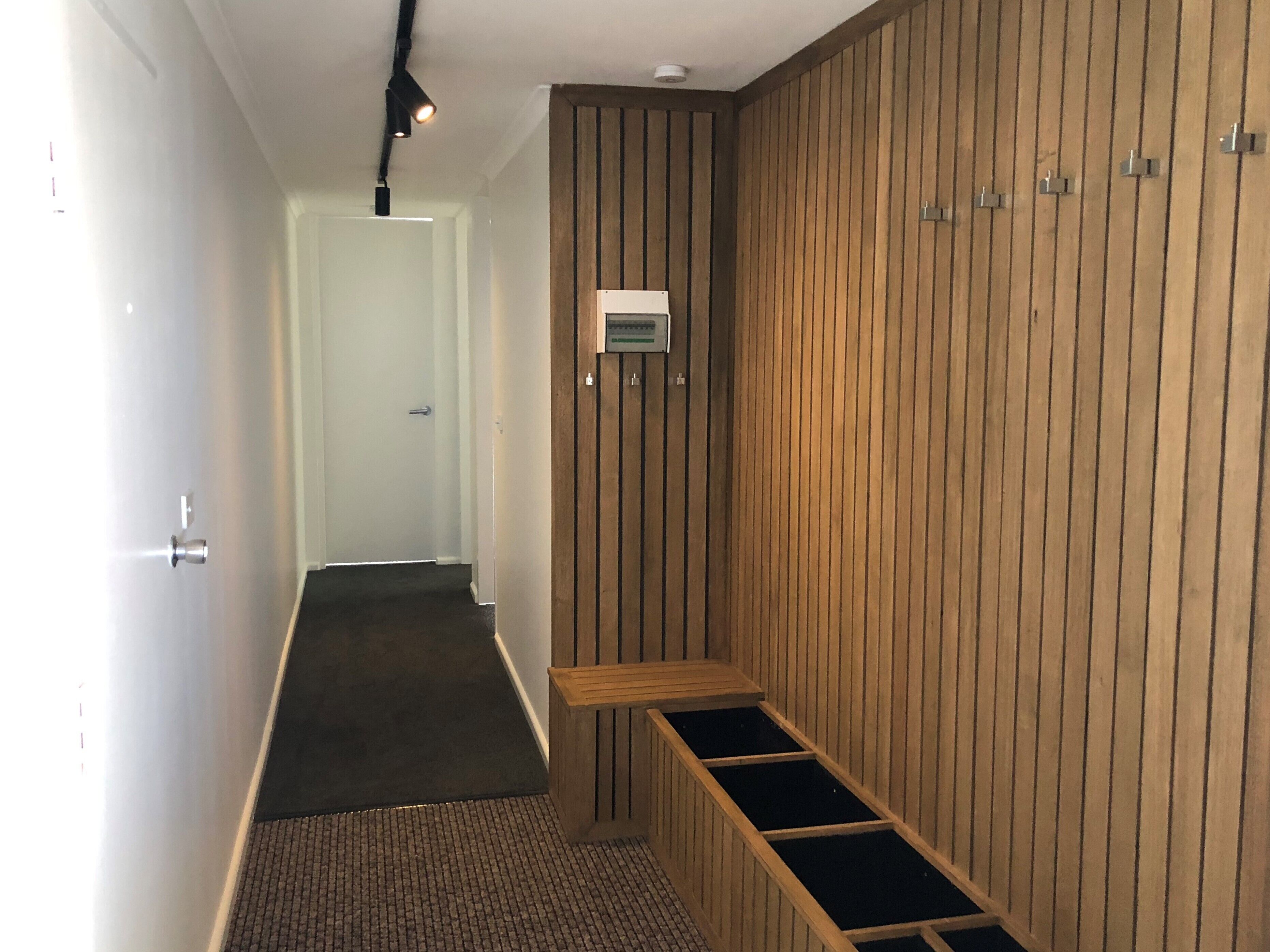 Un couloir avec un mur en bois, un banc et une porte au fond.