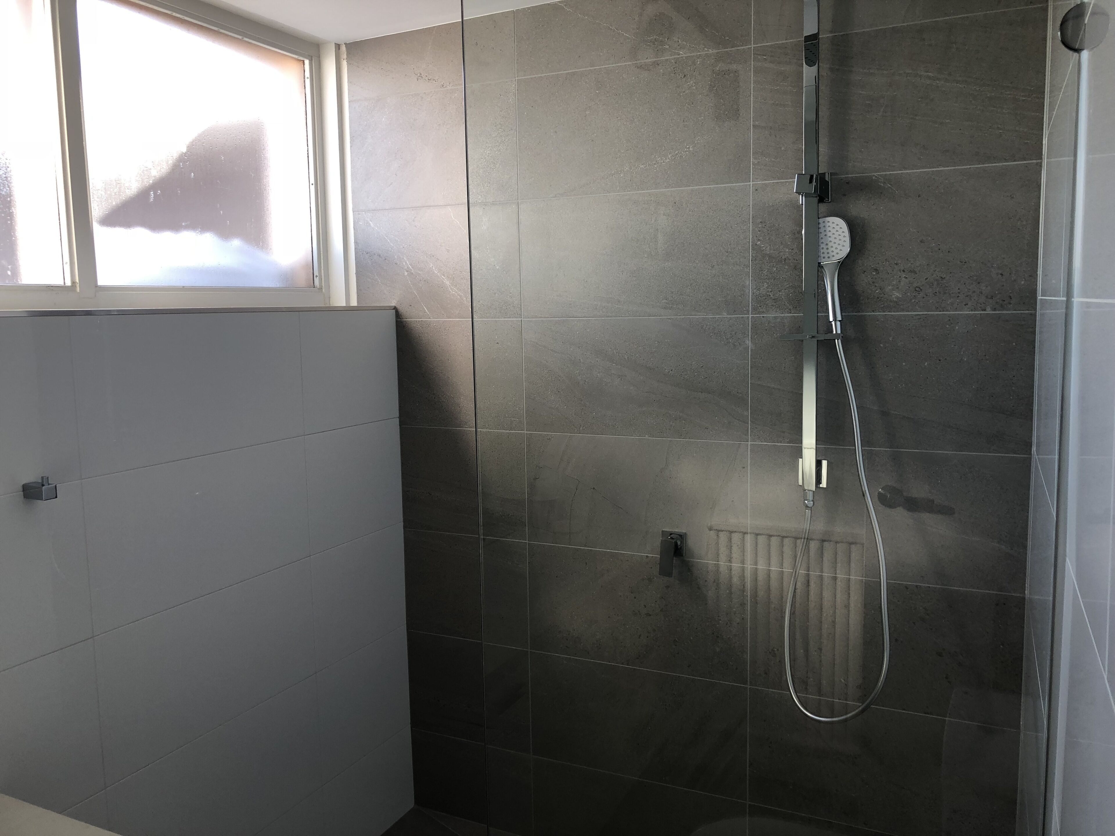 A modern bathroom with a shower, a window, and a radiator.