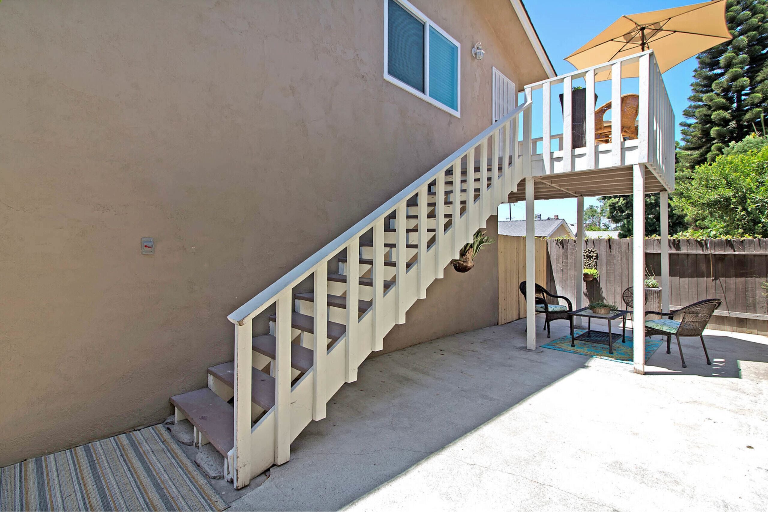 A house with a wooden staircase leading to a covered patio area with outdoor furniture.
