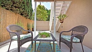 A patio with wicker furniture, a glass table, and a patterned rug.