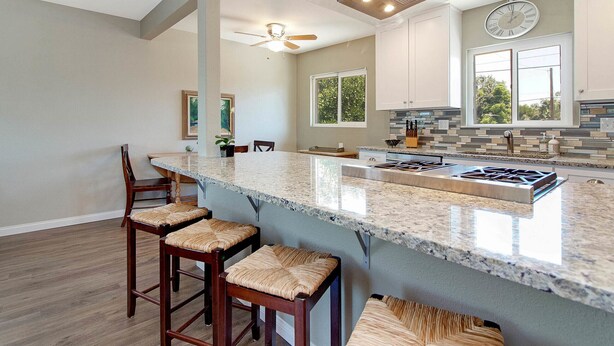A modern kitchen with a large island, bar stools, and a ceiling fan.