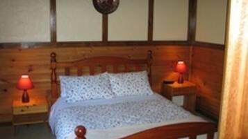 A wooden-framed bed with a patterned bedspread, two bedside lamps, and a wooden headboard.