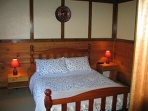 A wooden-framed bed with a patterned bedspread, two bedside lamps, and a wooden headboard. - Alpine Stag Lodge House (Merrijig)